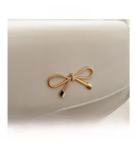 Close-up of elegant gold bow metal buckle on a white leather handbag with neat stitching