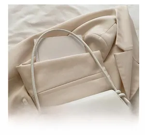 Close-up of white PU leather shoulder bag with golden bow clasp on beige blazer