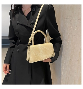 Chic beige crossbody flap bag worn with a black wool coat against a stone wall