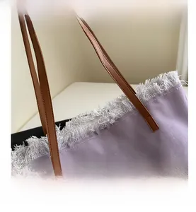 Detail view of purple canvas tote bag featuring raw fringe edges and brown faux leather straps