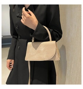 Detail of apricot suede crossbody bag with gold hardware worn on model shoulder