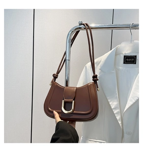 Close-up of brown leather underarm bag featuring a metallic U-shaped buckle and strap detail