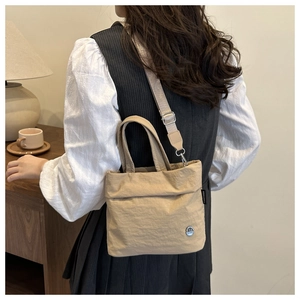 Borsa a tracolla minimalista in tela kaki indossata a spalla in un interno accogliente.