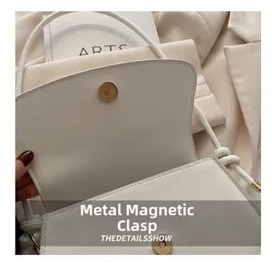 Close-up of golden magnetic snap closure on a minimalist white leather handbag