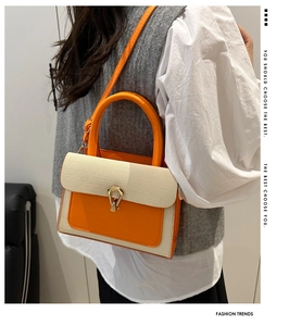 Detail of a chic orange leather and beige fabric crossbody bag with gold clasp buckle