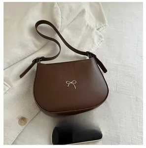 Detail of dark brown crescent underarm bag with silver bow accent on corduroy base