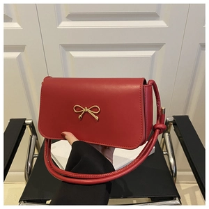 Détail du sac bandoulière en cuir rouge avec boucle métallique en forme de nœud doré