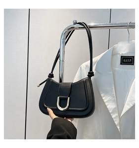 Minimalist black baguette bag with gold U-shaped metal buckle on a white blazer