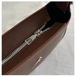 Close-up of smooth silver metal zipper and stitching on dark brown leather handbag
