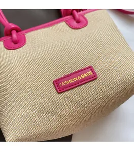 Détail du sac cabas en paille tissée avec anses en cuir fuchsia et logo doré