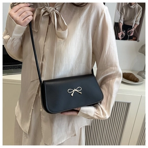Détail du sac à bandoulière noir élégant avec boucle nœud doré porté par un mannequin