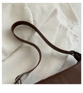 Detail of brown leather handle with stitching and silver metal buckle on shoulder bag