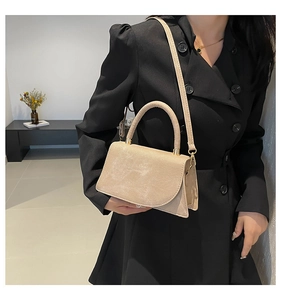 Detail of beige faux leather crossbody bag with golden hardware and elegant curved flap