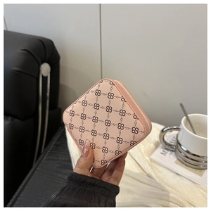 Nahaufnahme einer rosa Schmuckschatulle mit Monogramm-Muster in der Hand.