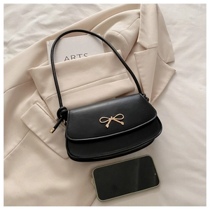 Close-up of black crossbody bag with golden bow buckle on beige suit background