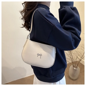 Woman wearing a minimalist white crescent underarm bag with silver bow detail on blue hoodie