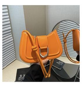 Close-up of orange leather crossbody bag featuring a silver U-shaped metal buckle and knot strap