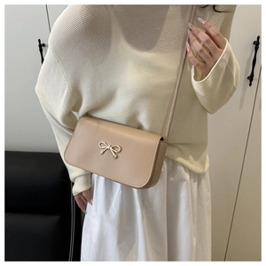 Détail d'un sac bandoulière beige à nœud assorti à une tenue blanche pour un style élégant