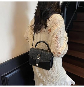 Détail du sac bandoulière noir avec texture croco et boucle cœur dorée sur le mannequin