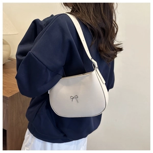 Close-up of cream underarm bag with silver bow detail on a stylish model in home setting