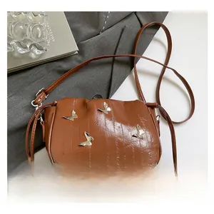 Detail of retro brown leather crossbody bag featuring silver butterfly hardware accents