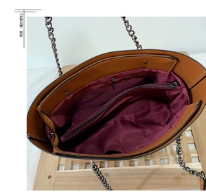 Macro view of a brown leather tote bag interior with red lining and metal chain strap