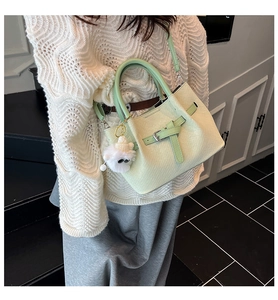 Detail of light green woven texture bucket bag with plush monster charm and top handles