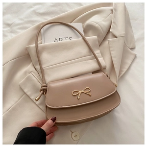 Close-up of golden bow hardware on apricot saddle bag with smooth PU leather texture