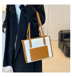 Detail of checkered woven tote bag with brown leather trim and golden metal accent