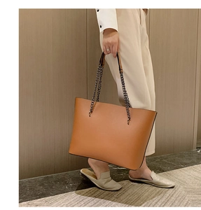 Detail of a large brown leather tote bag with elegant gold chain straps and smooth finish