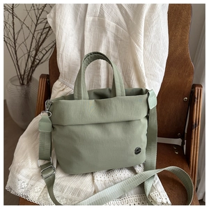 Dettaglio della borsa di tela verde su sedia in legno con abito vintage sullo sfondo.