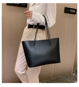 Model wearing a black matte leather tote bag with stylish metal chain strap indoors
