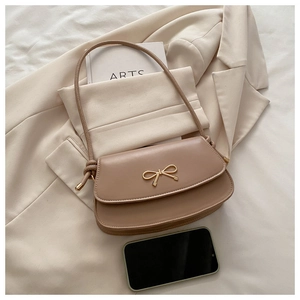 Detail of elegant bow metal buckle and thin leather strap on a beige flap handbag