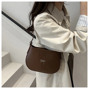 Close-up of brown crescent underarm bag with silver bow on a beige trench coat