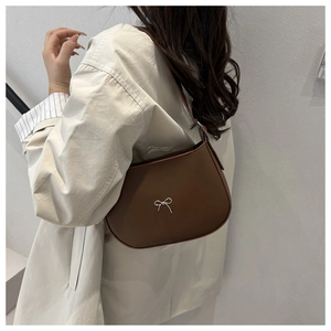 Brown leather hobo shoulder bag with silver metal bow detail on a female model