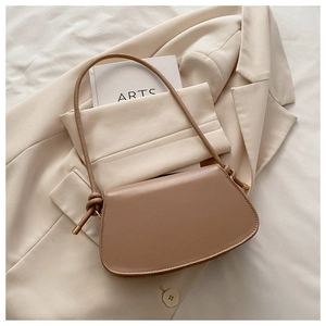 Close-up of minimalist beige leather handbag with decorative knotted strap and metal tips