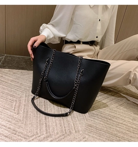Chic black leather tote bag with chain strap shown in a stylish minimalist setting