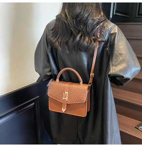 Détail d'un sac bandoulière marron motif crocodile avec boucle dorée porté à l'épaule