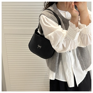 Detail of a black crescent shoulder bag featuring a silver bow on a white shirt