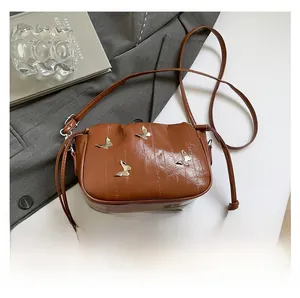 Detailed view of brown glossy leather crossbody bag with silver butterfly charms and drawstring