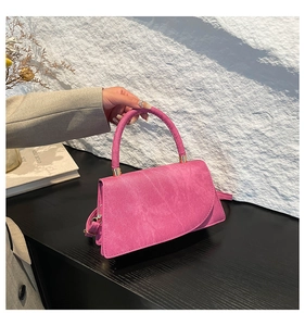 Detail of rose pink suede handbag with gold buckle and matching round handle on table