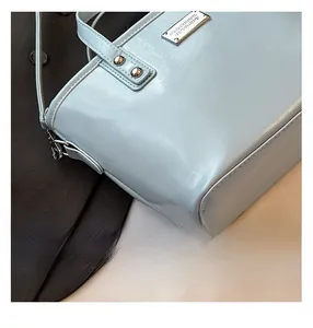 Detail view of light blue leather bucket bag with silver metal logo and refined texture