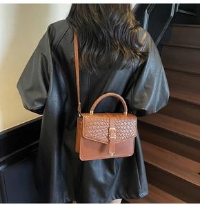 Détail du sac bandoulière marron tressé avec boucle cœur sur veste en cuir