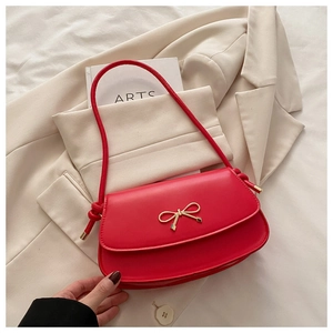 Detail of red crossbody bag featuring a golden bow buckle on a beige blazer backdrop