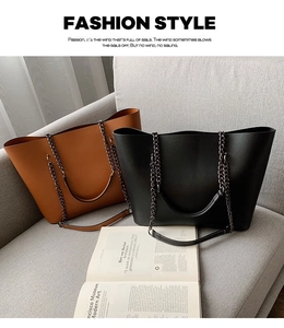 Detail view of black and caramel brown tote bags with metal chain straps on a gray sofa