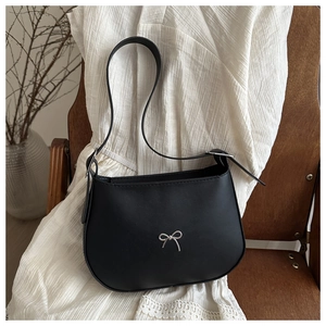 Close-up of black leather underarm bag featuring a silver metal bow on a wooden chair