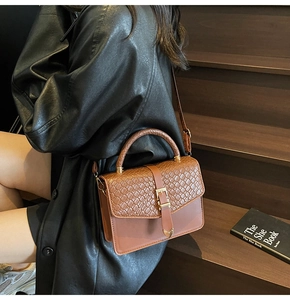 Détail de la texture tissée et boucle dorée sur un sac bandoulière en cuir brun