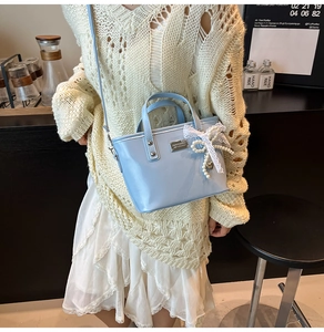 Close-up of light blue bucket bag featuring white lace bow and pearl charm detail