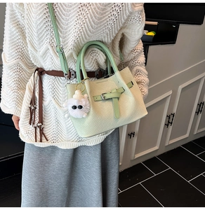 Detail of mint green bucket bag with woven texture, shoulder strap and plush charm