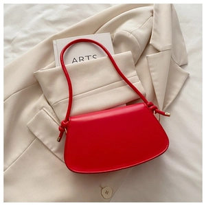 Detail of red leather crossbody bag featuring a unique knotted handle and gold metal buckles
